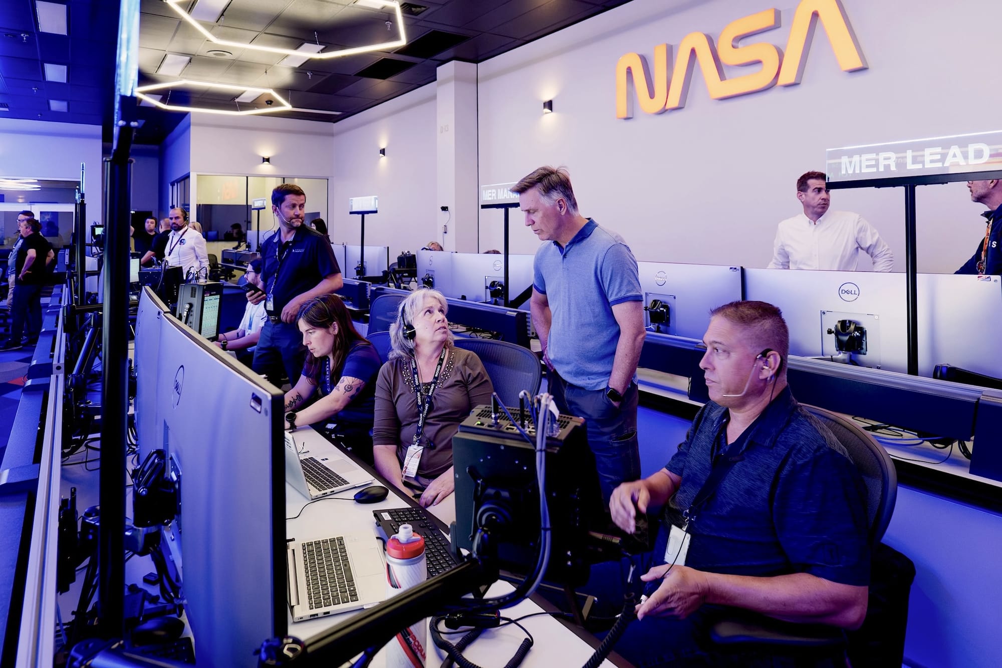 Multiple people working on consoles in a space-mission-control like room at a NASA facility.