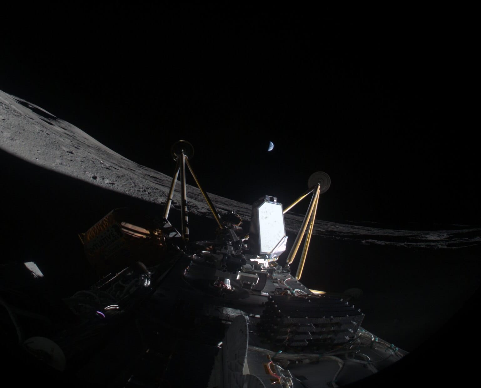 The Athena CLPS lander is seen lying on its side inside a shadowed crater after its hard landing. Two of its legs are visible, with the Earth half-lit hanging above in the black sky.